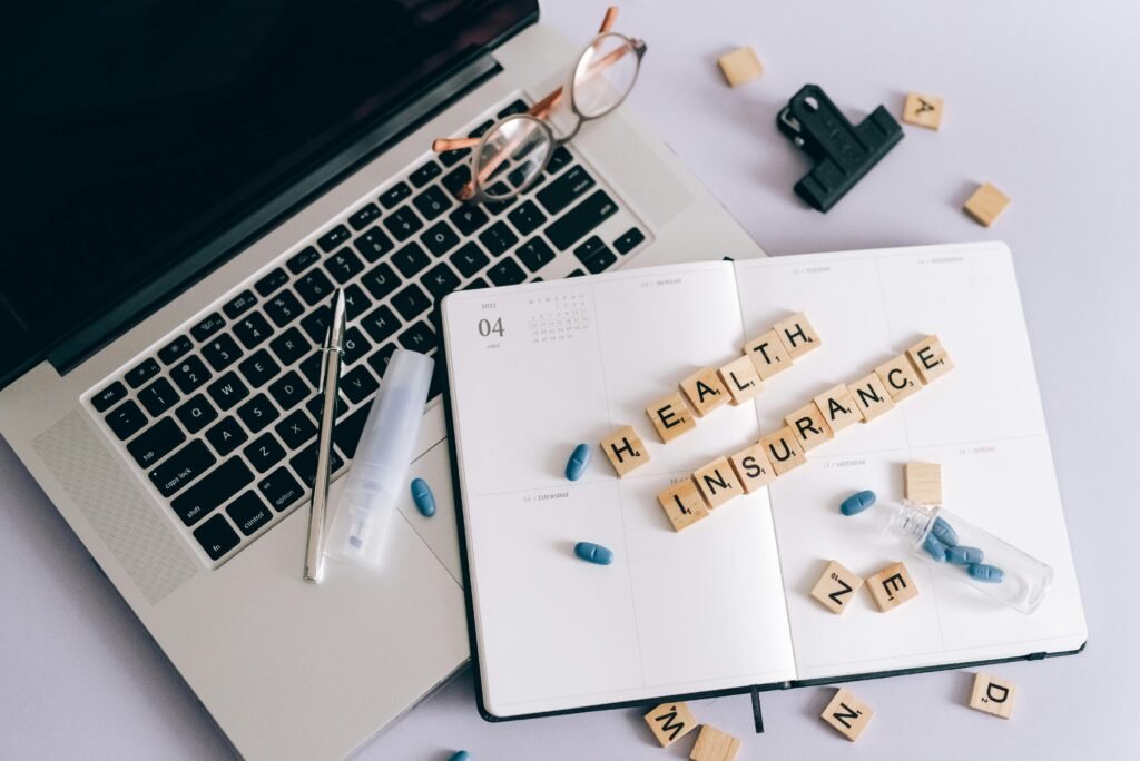 pexels-photo-7163950-7163950 Flat lay of a laptop, notebook, and pills depicting health insurance planning.